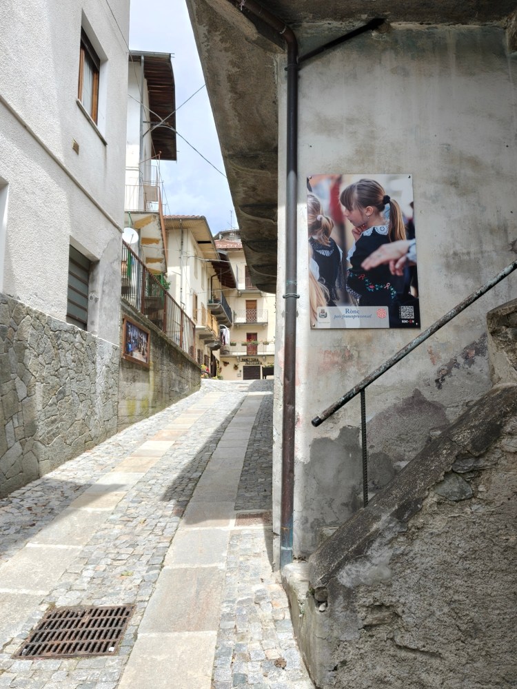 Una strada acciottolata in un paesino, con edifici bianchi e una parete con un poster che ritrae una bambina.