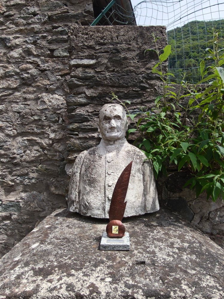 Un busto di pietra di un uomo, situato su un muro di pietra, con una statua a forma di penna in primo piano.