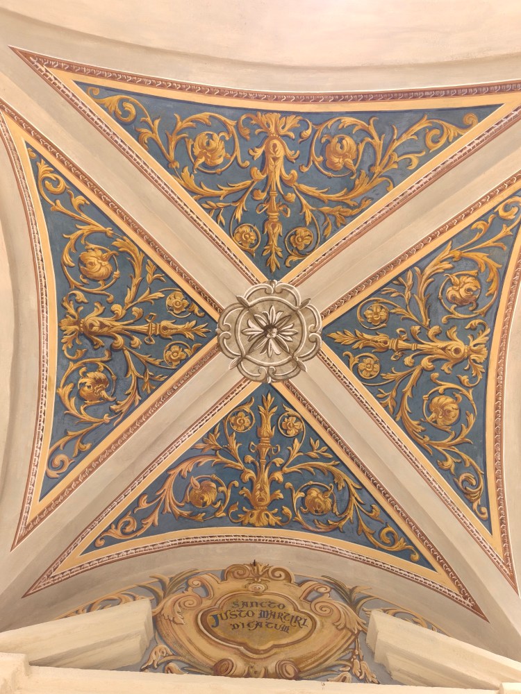 Soffitto decorato con motivi floreali in oro e blu, con un motivo centrale rotondo e un'iscrizione sottostante.