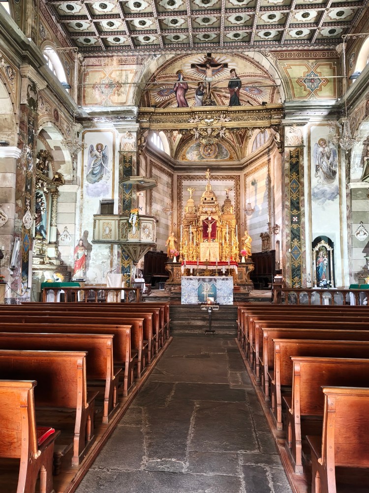 Interno di una chiesa con panche in legno, altare dorato e affreschi sulle pareti e sul soffitto.