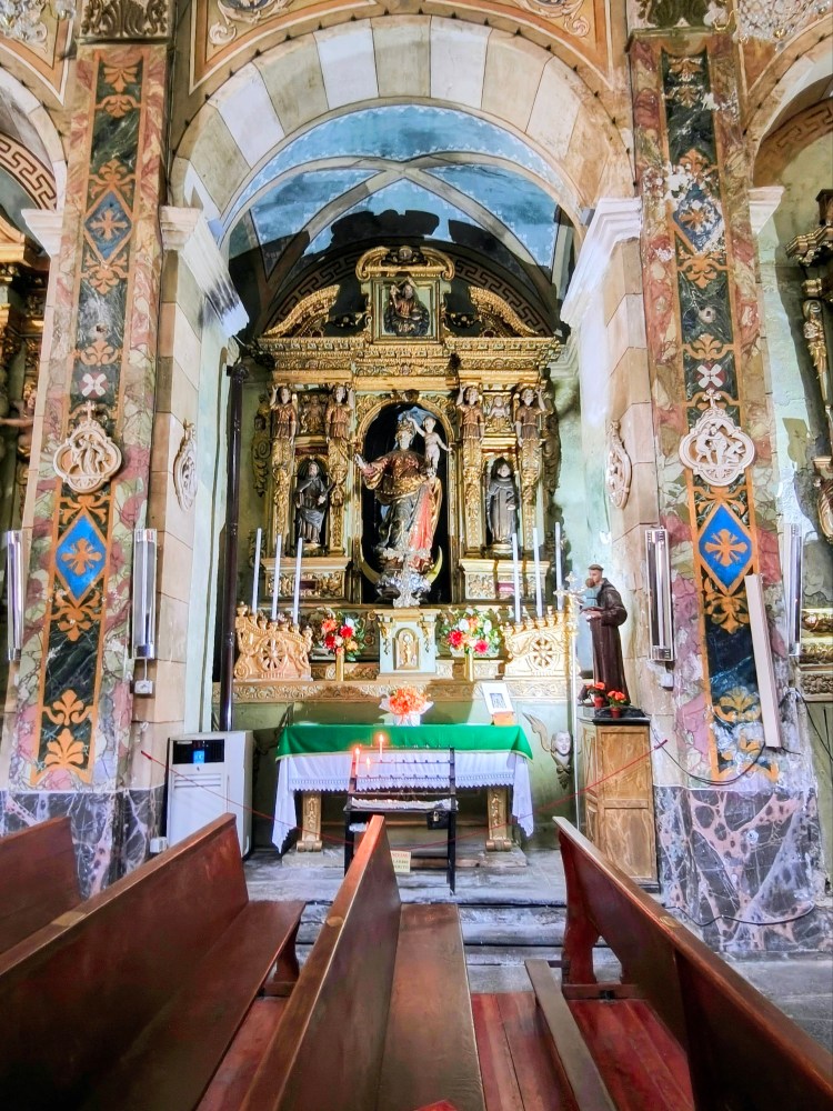 Interno di una chiesa con un altare decorato e candele accese, circondato da panche di legno.