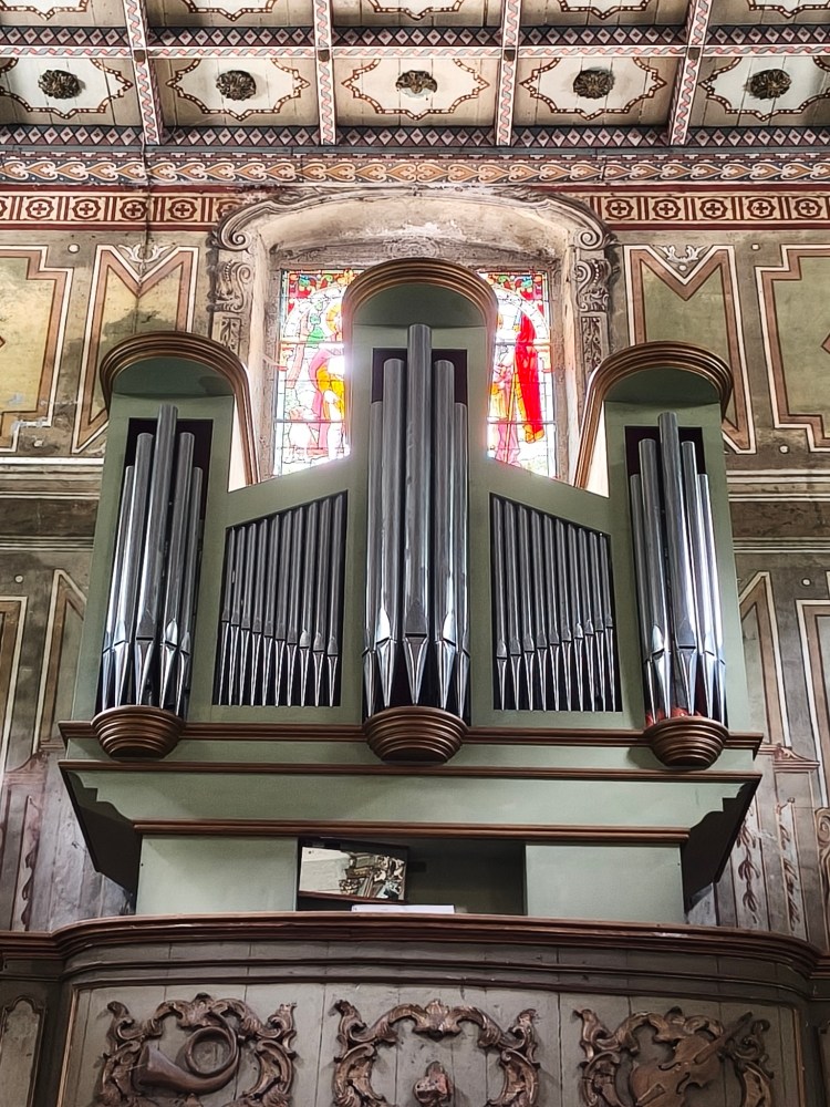 Organo a canne di un'architettura ecclesiastica, con dettagli decorativi e vetri colorati sullo sfondo.