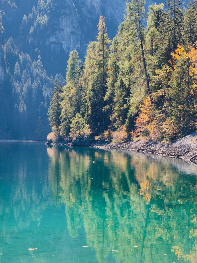 Lago circondato da alberi verdi e arancioni, con riflessi sull'acqua.
