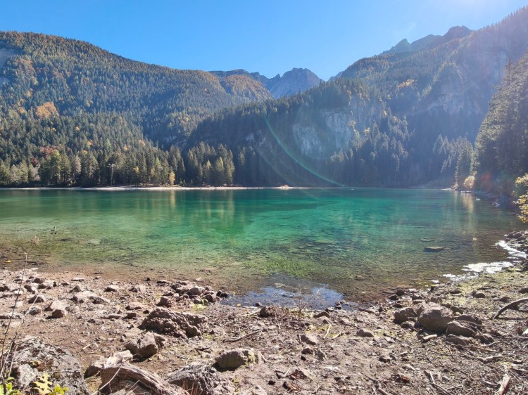 Un lago cristallino circondato da montagne e foreste colorate da alberi in autunno.