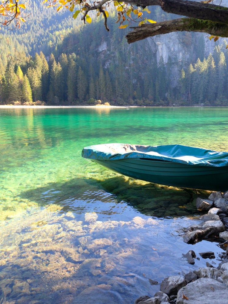 Un'imbarcazione verde ancorata su un'acqua cristallina, circondata da foreste e montagne, con rocce visibili sul fondale.