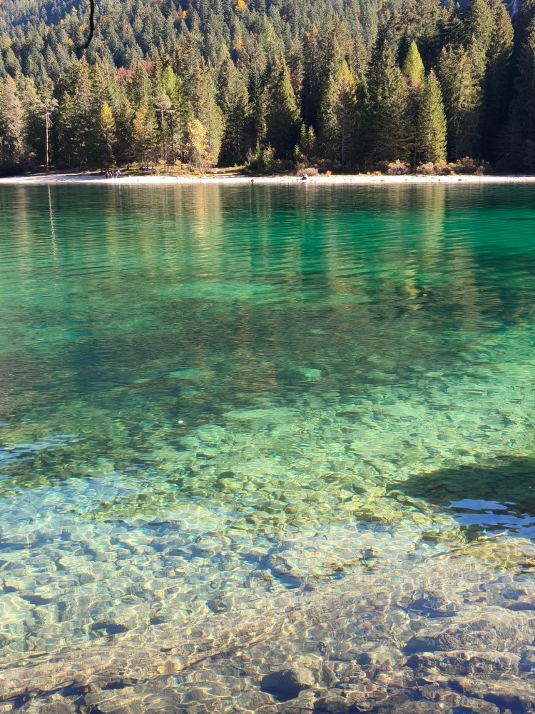 Un lago con acque cristalline e verde smeraldo, circondato da alberi e montagne.