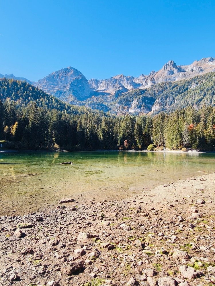Lago circondato da montagne verdi e rocciose sotto un cielo blu sereno.