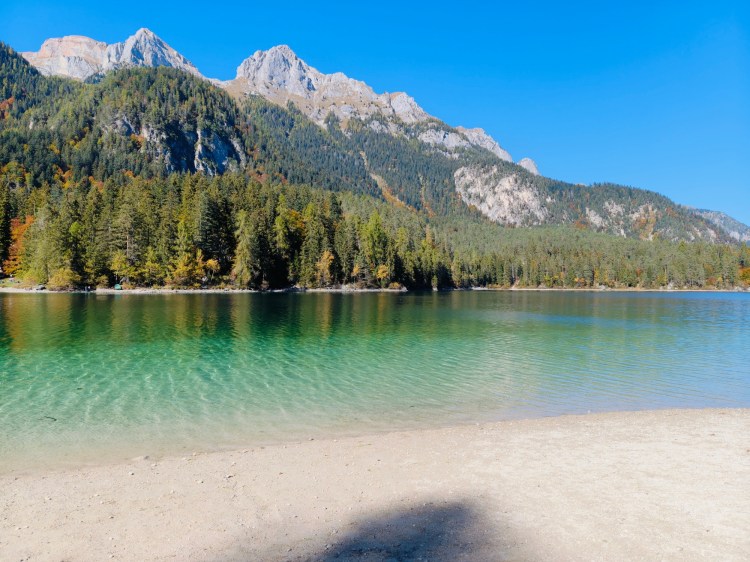 Un lago tranquillo circondato da alberi e montagne, con acqua cristallina e un cielo sereno.