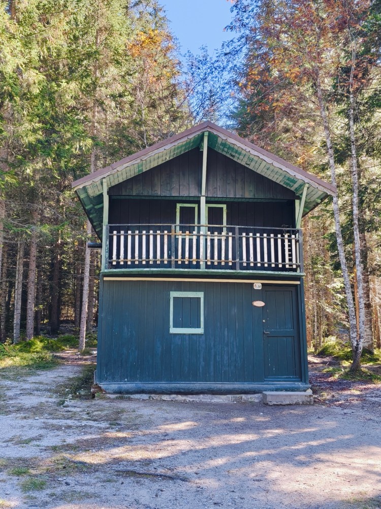 Una casa di legno a due piani immersa in un bosco, con un balcone e un ingresso sul lato.