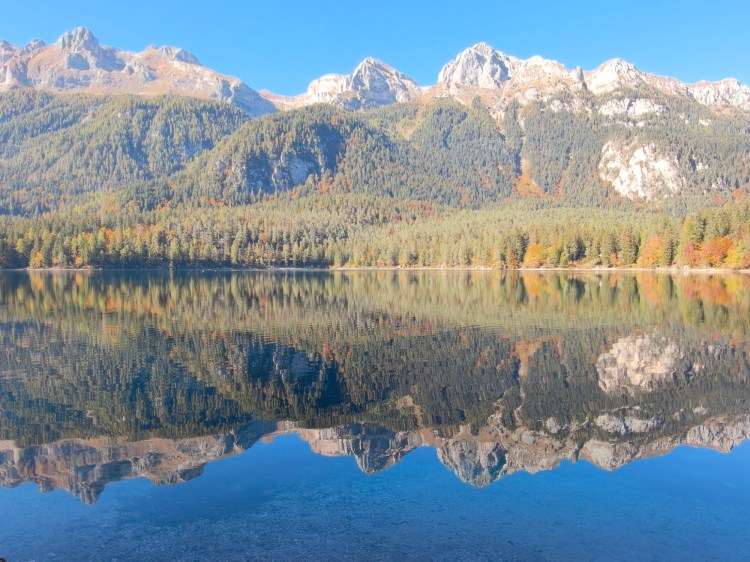 Un lago sereno circondato da montagne maestose con riflessi sulla superficie dell'acqua.