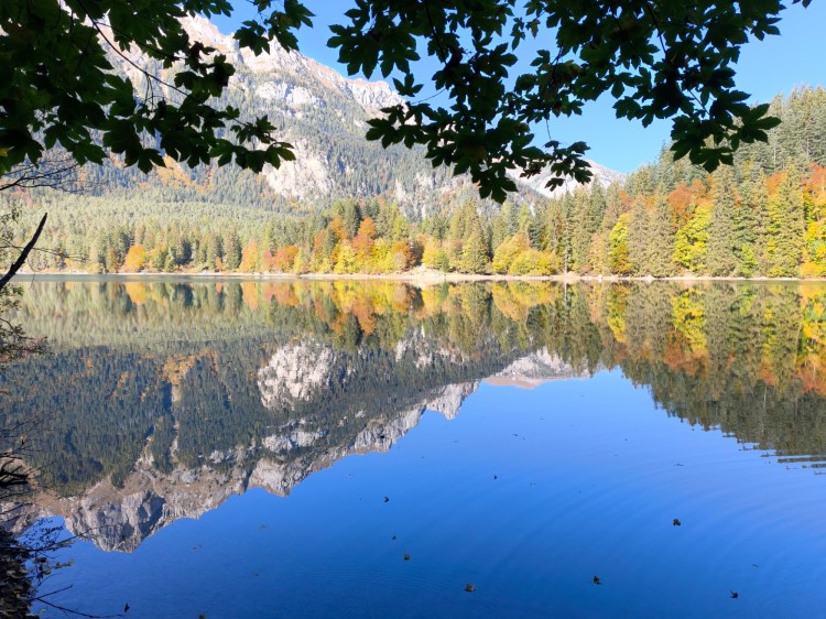 Vista serena di un lago circondato da montagne e alberi, con riflessi vivaci sull'acqua.