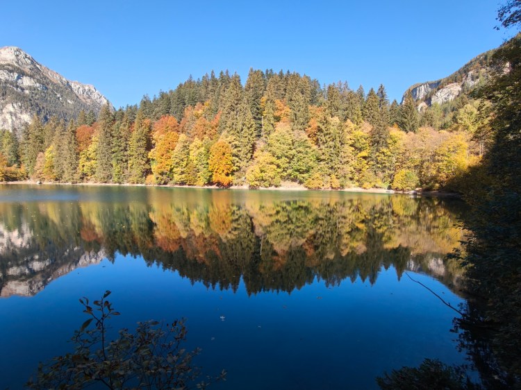 Vista di un lago circondato da alberi colorati in autunno, con un cielo blu limpido.
