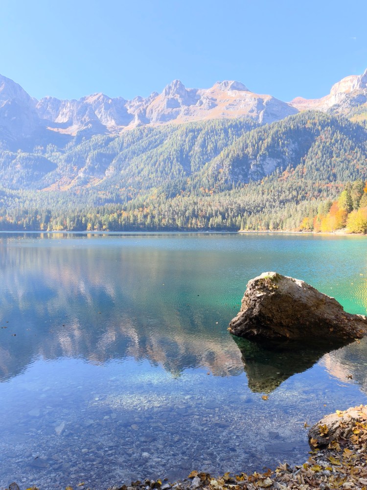 Un lago tranquillo circondato da montagne verdi e rocciose, con riflessi sull'acqua cristallina in un giorno soleggiato.