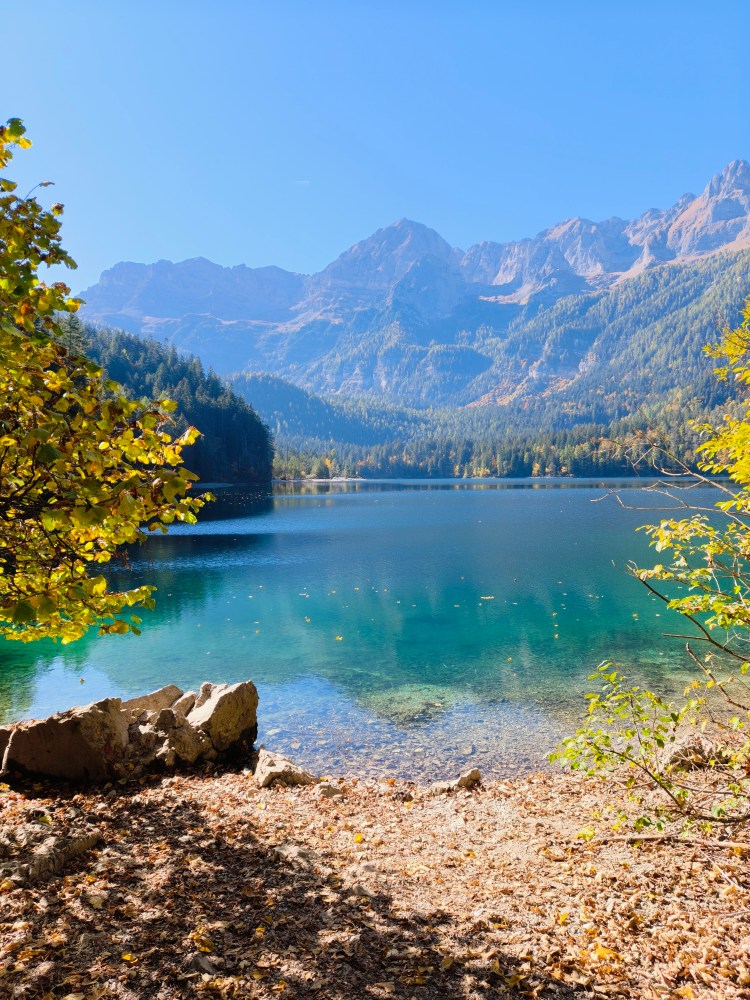 Vista di un lago cristallino circondato da montagne e alberi nel periodo autunnale.
